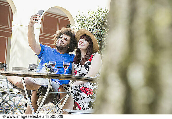 Young couple taking selfie using mobile phone camera at outdoor restaurant