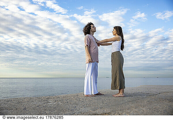 Young couple touching each other standing on pier by sea