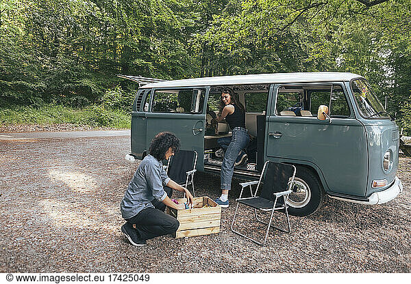 Young couple unloading luggage from van during camping