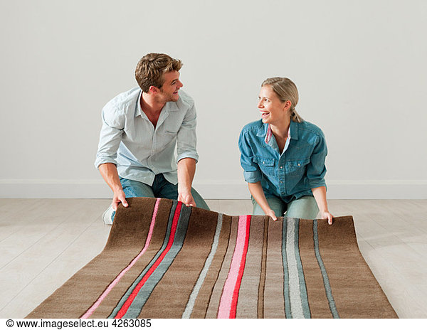 Young couple unrolling rug on floor