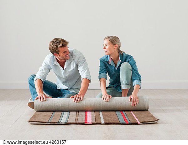 Young couple unrolling rug on floor