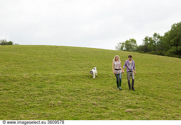 Young couple walking down hill with dog