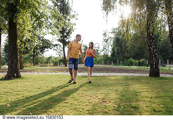 Young couple walking hand-in-hand to go play badminton in the park