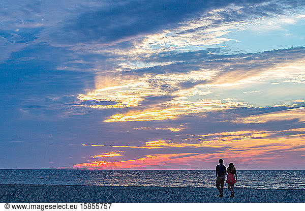 Young couple walking on beach admiring beautiful sunset.