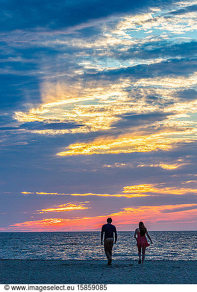 Young couple walking toward ocean during colorful sunset.