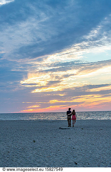 Young couple walking toward ocean under beautiful sunset sky colors.