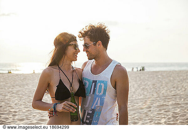 Young couple with arms around looking at each other on beach