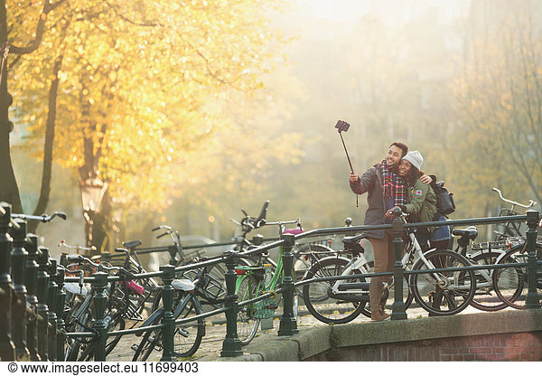 Young couple with bicycles taking selfie with selfie stick on autumn bridge  Amsterdam