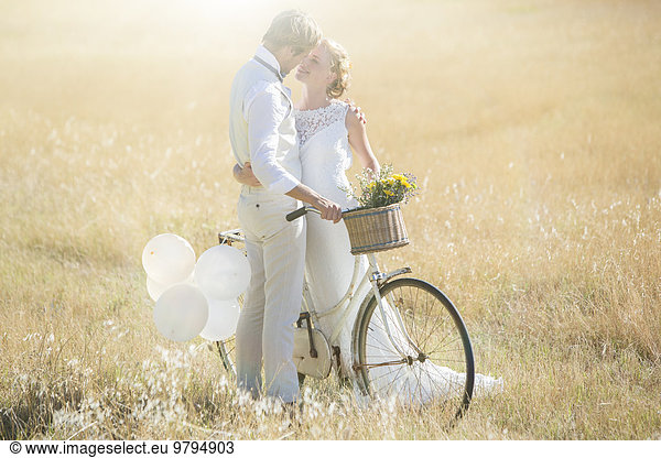 Young couple with bike kissing in meadow