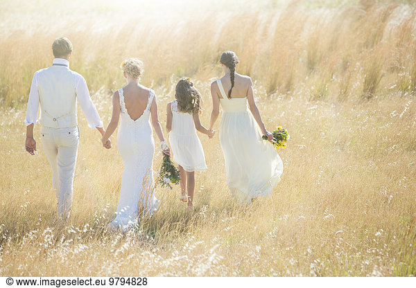 Young couple with bridesmaid and girl walking in meadow