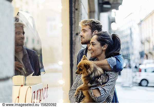 Young couple with dog looking in shop window in the city