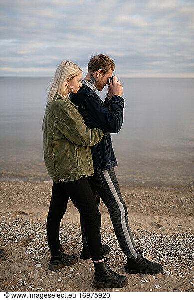 Young couple with photo camera standing on lake shore