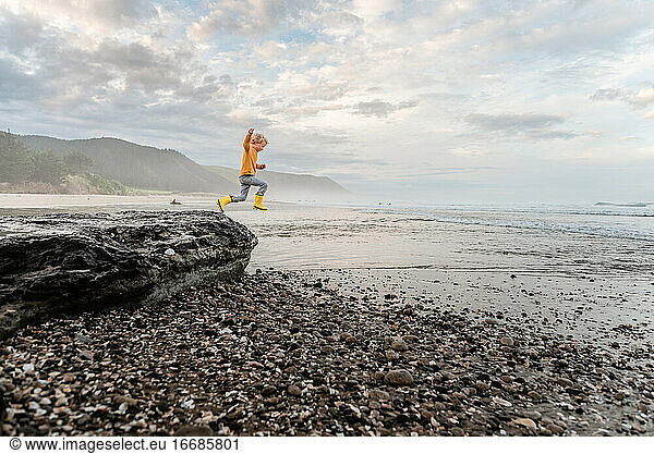 Young curly haired child leaping from rock at beach in New Zealand