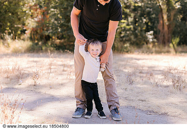 Young dad standing  toddler between legs  holding hands