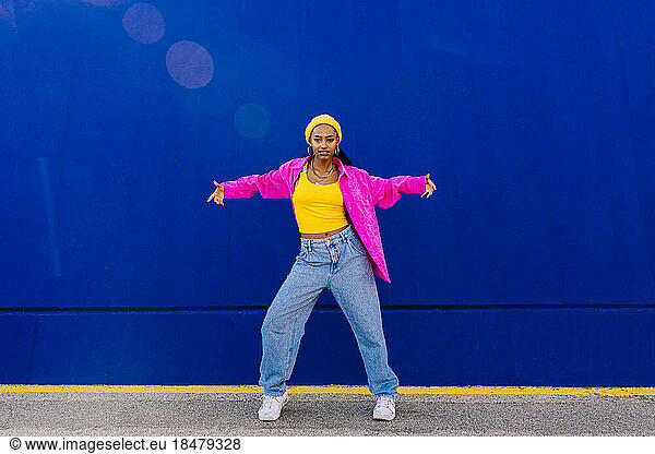 Young dancer with arms outstretched dancing in front of blue wall