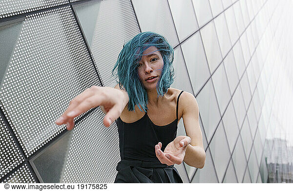 Young dancer with blue dyed hair dancing in front of modern building