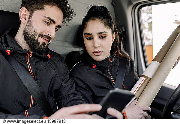 Young delivery man and woman using mobile phone in truck