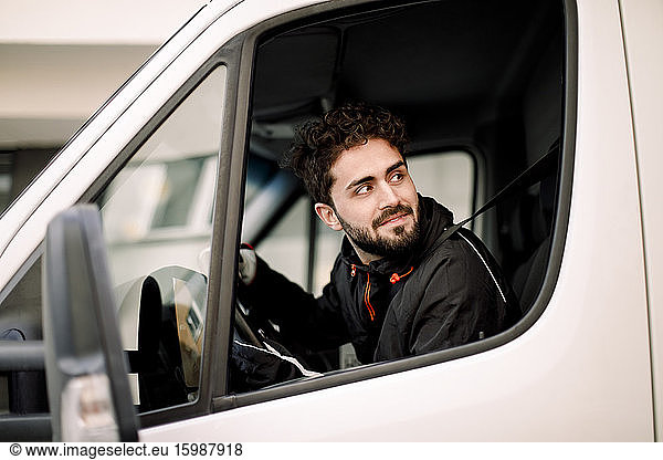 Young delivery man looking through window while driving truck