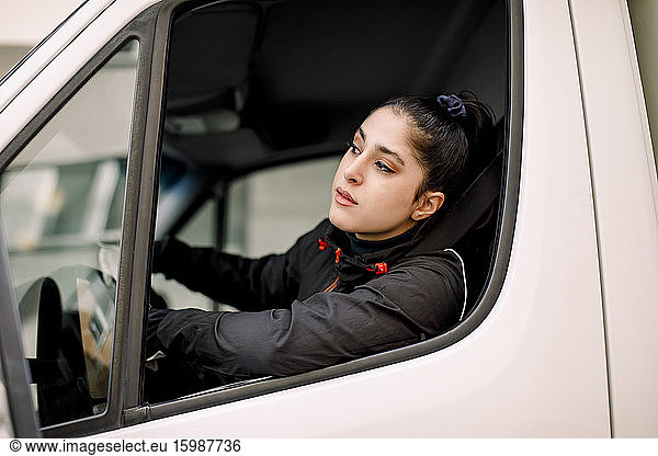 Young delivery woman looking through window while driving truck