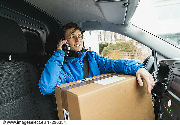 Young delivery woman talking on mobile phone while sitting with package in van