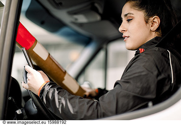 Young delivery woman using smart phone while driving truck