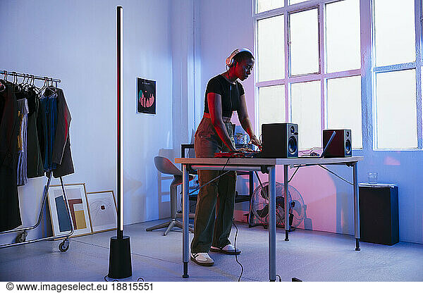 Young DJ wearing headphones and using laptop at home