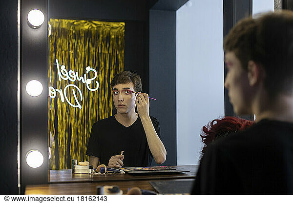 Young drag queen applying eyeshadow looking at mirror in dressing room