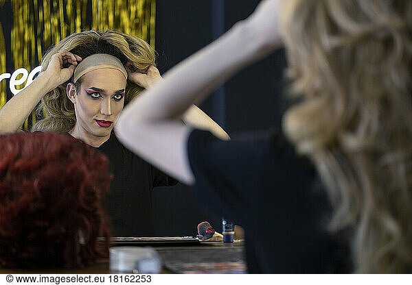 Young drag queen wearing wig looking at mirror in dressing room