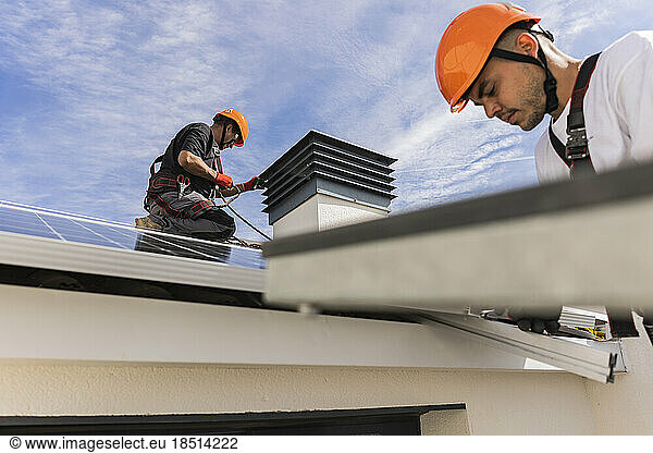 Young engineer wearing hardhat installing solar panels with colleague