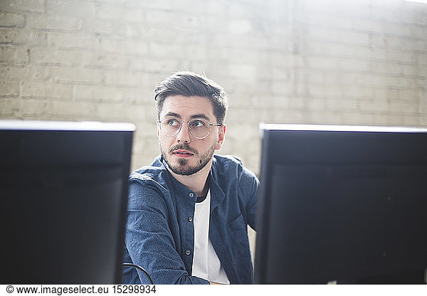 Young entrepreneur looking away while working on computer programs in creative office