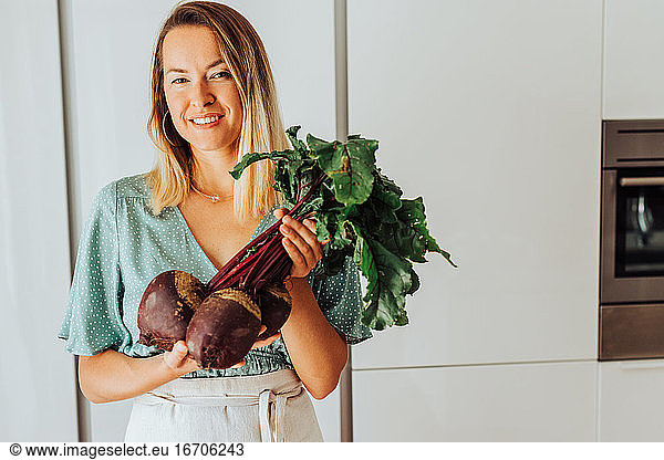 Young European woman holding beetroot while smiling at camera