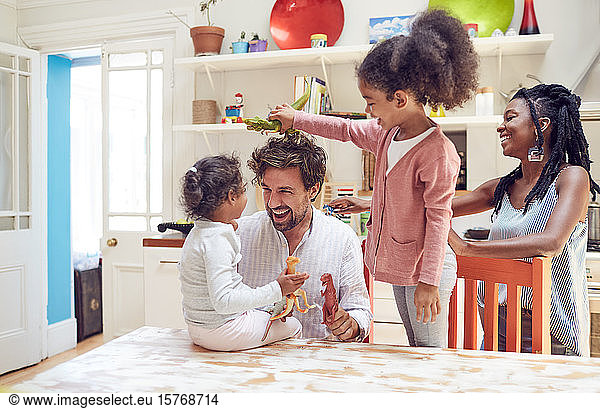 Young family playing with toy dinosaurs in kitchen