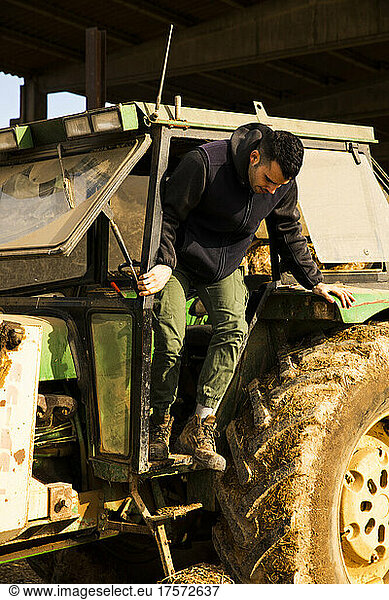 Young farmer boy getting off the tractor while working on the farm
