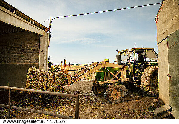 Young farmer boy loading a bale of straw with the tractor