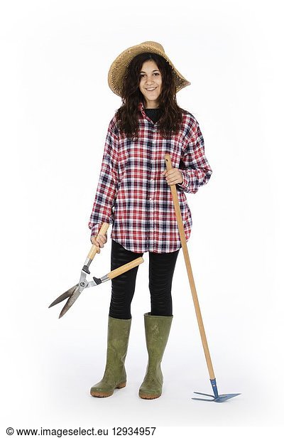 Young farmer with shears and hoe in hands  she is wearing a straw hat  checked shirt and green rubber boots.