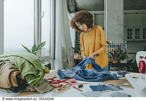 Young fashion designer cutting jeans with scissors in workshop