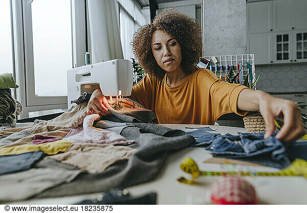 Young fashion designer sitting with clothes and sewing machine at table