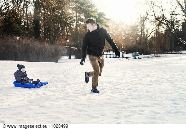 Young father tobogganing baby boy on snowy field