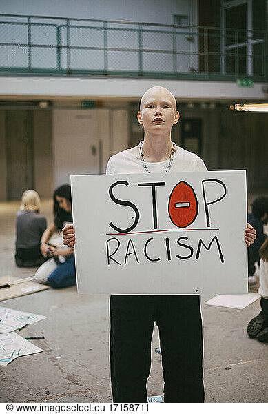 Young female activist with stop racism poster standing in building