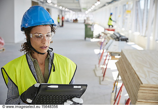 Young female architect in reflective clothing using digital tablet at construction site