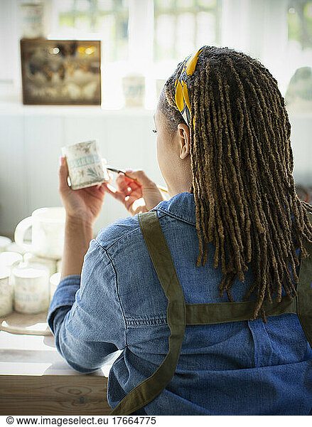 Young female artist painting ceramic mug