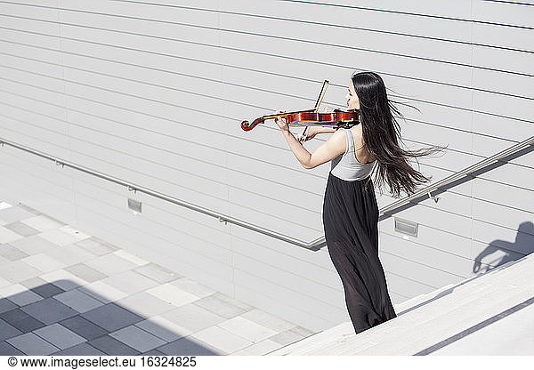 Young female Asian playing violin on stairs