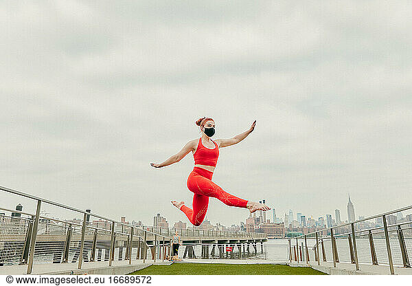 Young female athlete jumping mid air wearing face mask by waterfront