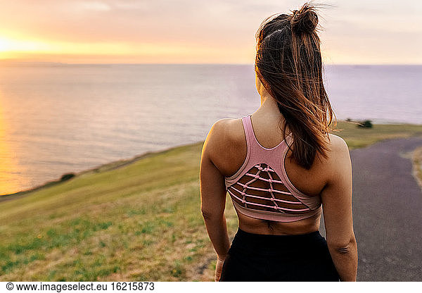 Young female athlete looking at sea during sunset
