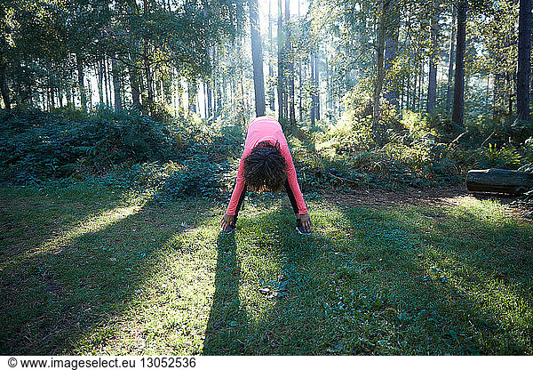 Young female bending forward stretching in forest