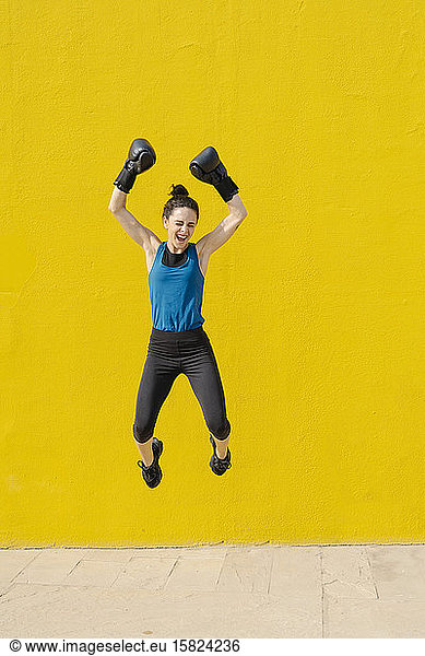 Young female boxer jumping in front of a yellow wall