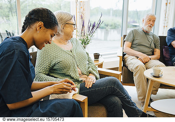 Young female caretaker filing senior woman's nail while sitting at nursing home