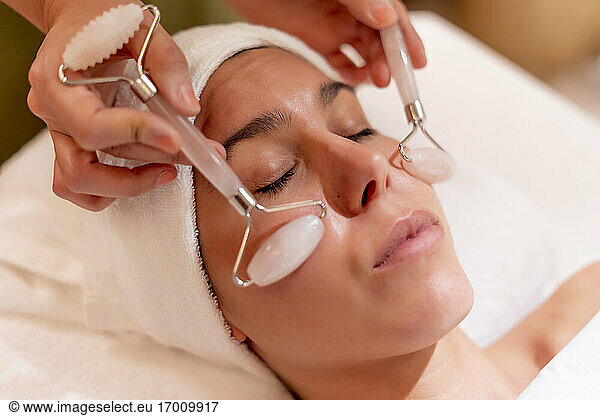 Young female customer receiving facial massage during spa treatment from beautician