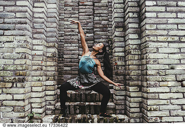 Young female dancer practicing dance amidst stone walls