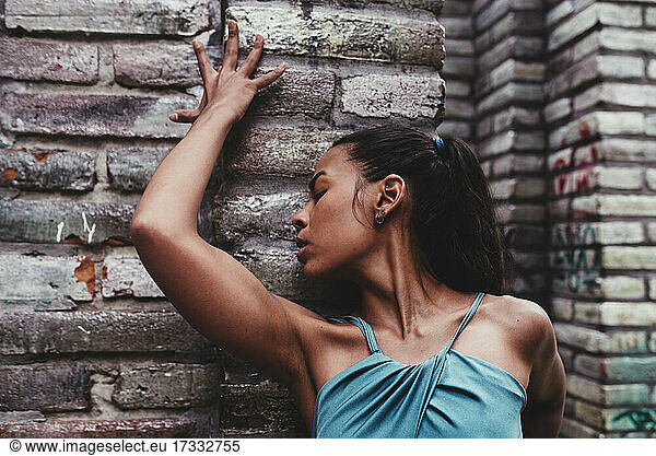 Young female dancer with eyes closed in front of stone wall